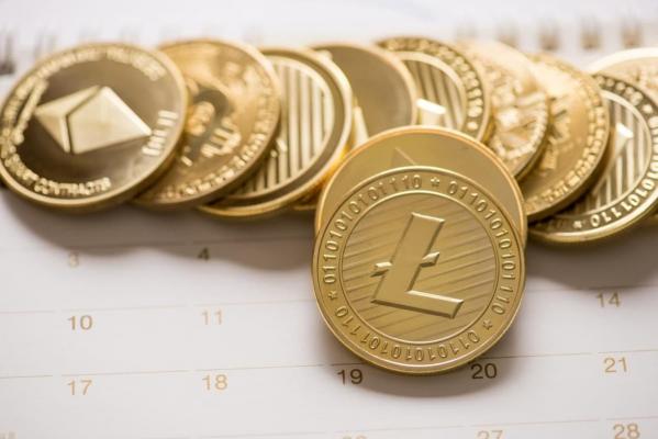 Una criptomoneda Litecoin junto a otras monedas digitales sobre un calendario.