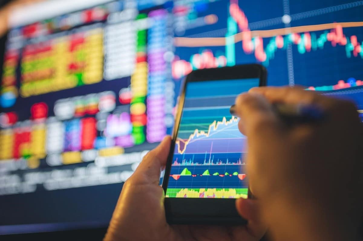 Un trader revisa en su celular tendencias de activos financieros para analizar en cuál conviene invertir.