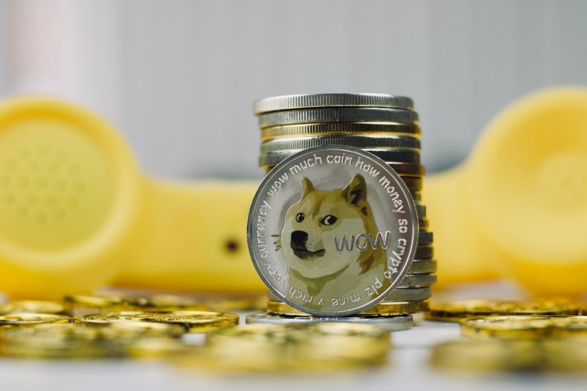 Una moneda DOGE y un teléfono al fondo. Conoce aquí cómo comprar Dogecoin en México.