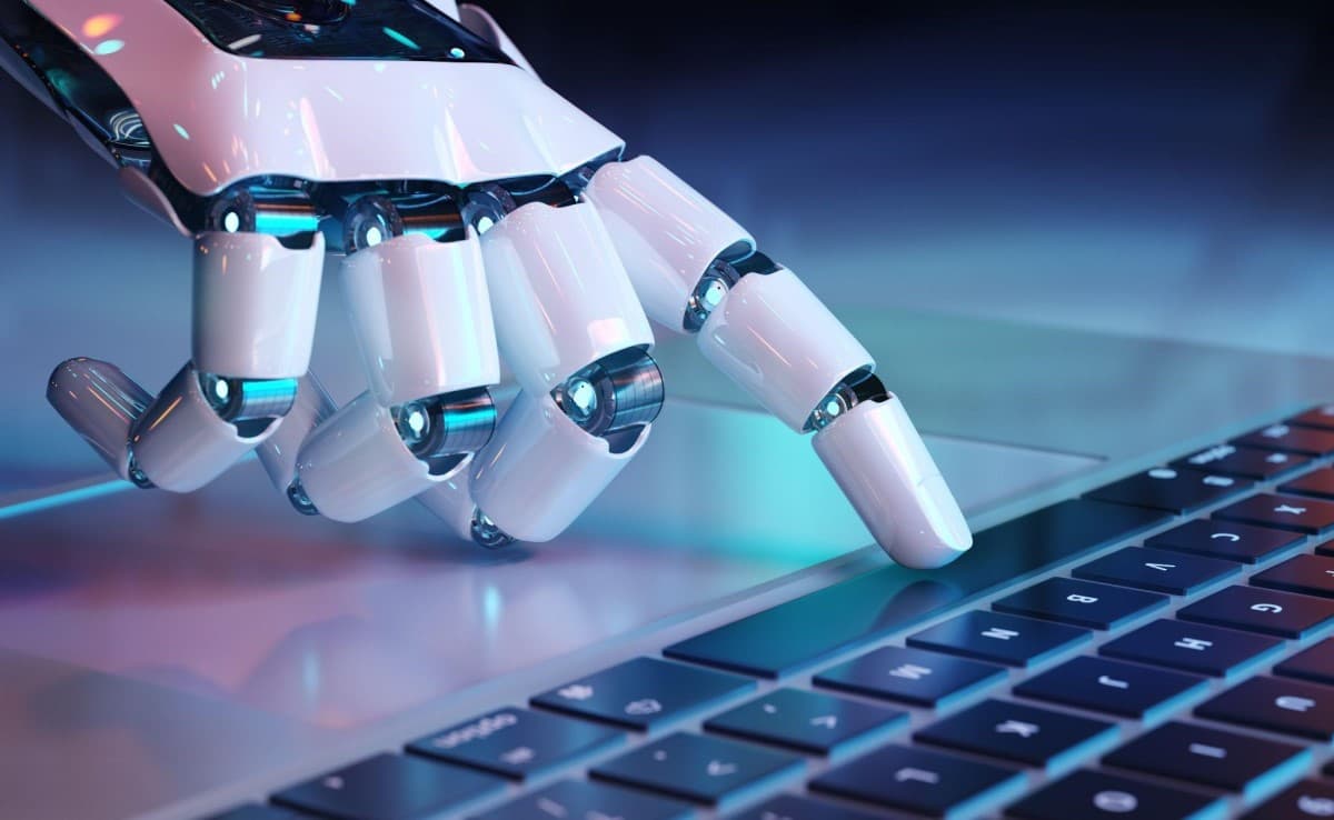 Mano de un robot sobre el teclado de un computador. Descubre acá las empresas de inteligencia artificial en Bolsa.