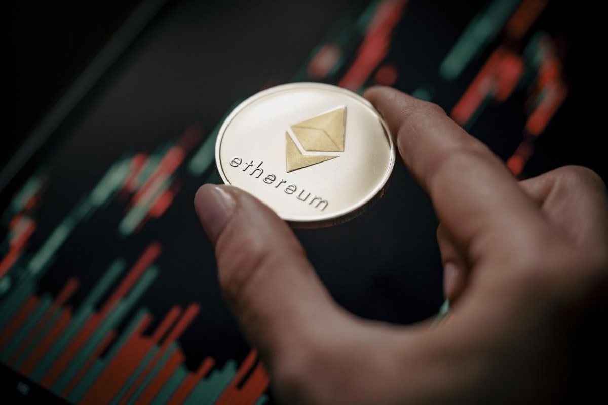 Un trader sostiene una moneda Ethereum en su mano con una gráfica de fondo.