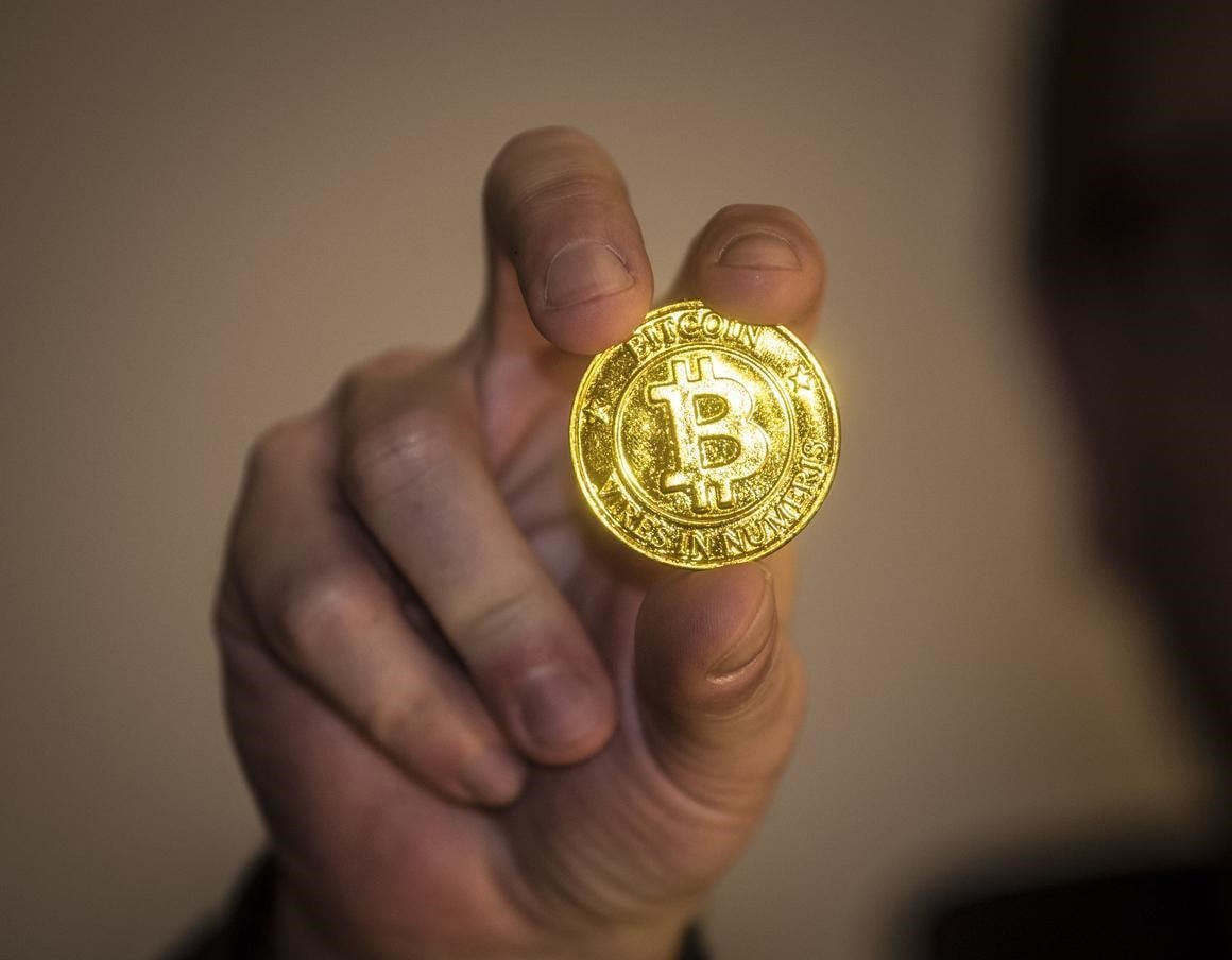 Un hombre sostiene en su mano una BTC. Aprende aquí a invertir en Bitcoin.