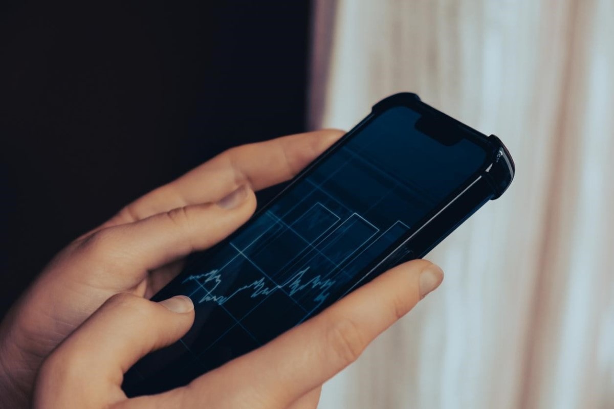 Una persona sostiene su celular y revisa gráficos de lo que son futuros en trading.