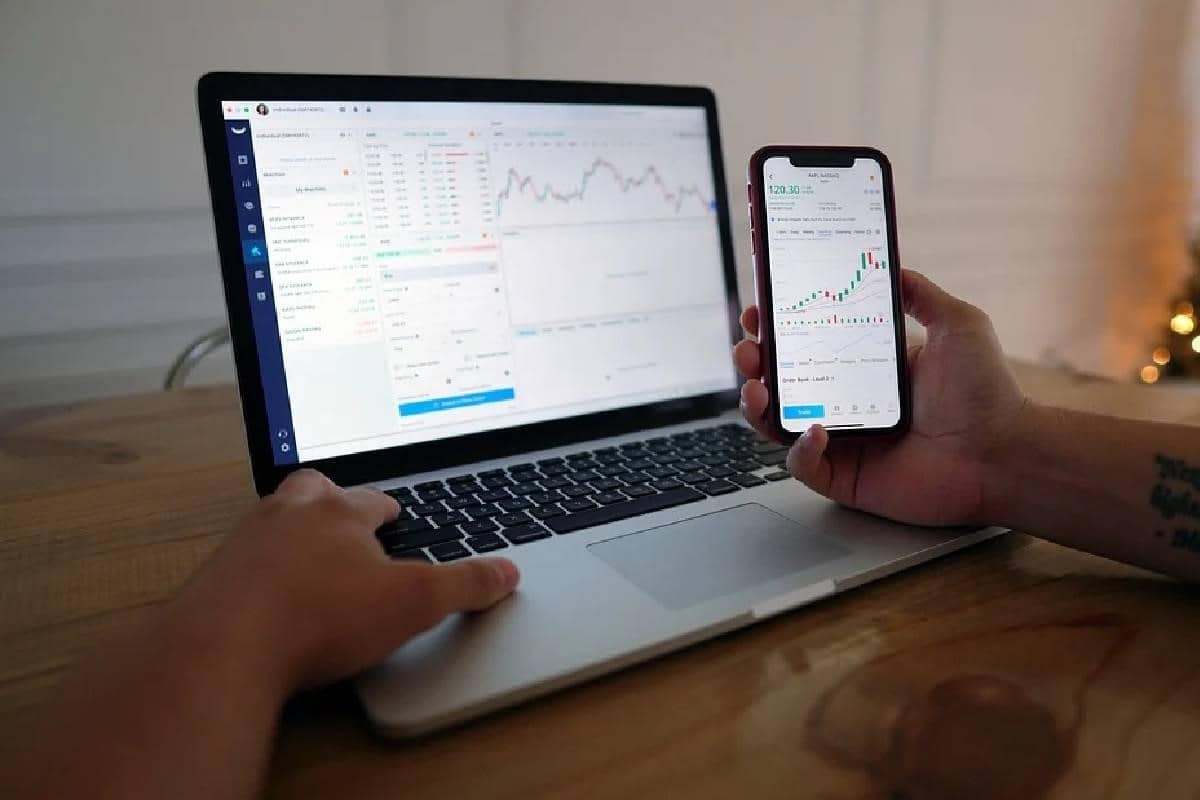 Un inversionista revisando gráficos en su computadora y celular. El trading algorítmico ayuda a que los traders no se pierdan ninguna inversión beneficiosa.