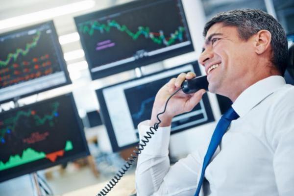 Corredor de bolsa sonríe mientras conversa por teléfono y analiza tendencias.