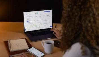 Una chica analiza el mercado en su computadora y compara con su celular. 