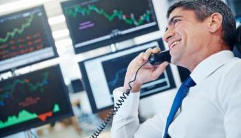 Corredor de bolsa sonríe mientras conversa por teléfono y analiza tendencias.