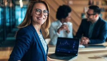 Una inversionista sonríe junto a su computadora, tras aplicar sus estrategias de trading con éxito.